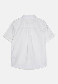 Camicetta bianca a maniche corte in cotone, con yoke sul retro, orlo dritto e tessuto morbido; senza motivi visibili o accessori.