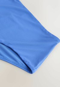 Prenda de baño de tela azul claro con textura suave, que presenta una sola costura y extremos curvados, mostrando un ligero brillo.