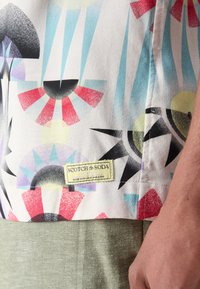 Košeľa s krátkym rukávom s farebným geometrickým vzorom v červenej, modrej, čiernej a žltej farbe; na ktorej je štítok "Scotch & Soda".