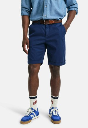 Shorts en coton bleu marine avec un ourlet retroussé, associés à des chaussettes blanches accentuées de bleu et de rouge, et des baskets bleues avec des rayures blanches.