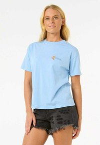 Lyseblå bomulds T-shirt med korte ærmer, med et lille blomster Rip Curl-logo på venstre bryst, parret med sorte slidte shorts.
