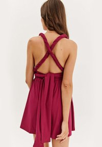 Bordová šaty s priliehavým pásom, rozšírenou sukňou a prekríženými lanovými ramienkami. Obsahujú viazaný akcent vzadu a hladkú textúru látky.