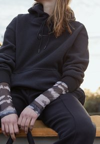 Černá fleecová mikina s kapucí a stahovací šňůrkou, doplněná o vzorované dlouhé rukávy v šedých a béžových tónech.