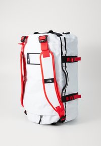 White backpack with red straps and accents, featuring a round shape, adjustable buckles, and a logo label on the side.