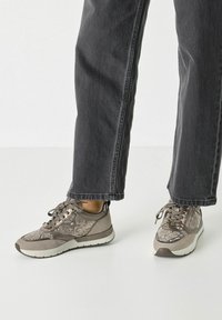 Des sneakers avec un dessus texturé gris et beige présentant un motif serpent, un bout rond et une semelle en caoutchouc blanc. Lacés avec des lacets gris assortis.