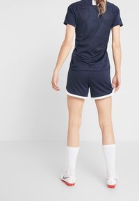 Marinträningsöverdel med korta ärmar och matchande shorts, båda med vita accenter. Bärs med vita strumpor och röda fotbollsskor.