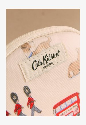 Textilcímke "Cath Kidston London" felirattal egy bézs neszesszeren, amely korgi kutyák, brit őrök és piros emeletes busz illusztrációit ábrázolja.