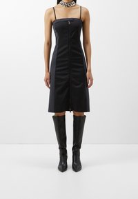 Sort midi kjole med lynlås foran, tynde stropper og en tætsiddende pasform. Kombineret med knæhøje sorte læderstøvler og et chunky kædenederdel.