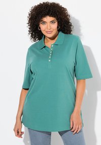 Polo shirt turchese con colletto, maniche corte e una chiusura con cinque bottoni. Texture liscia e una vestibilità rilassata con spacchi laterali.
