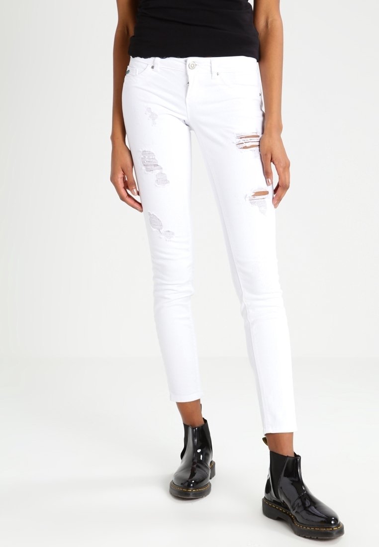 Jean skinny blanc avec détails usés et patches effilochés. Associé à des bottines noires brillantes avec une semelle épaisse et une fermeture éclair latérale.