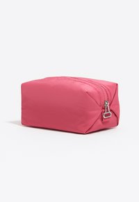 Bolsa rectangular rosa con cremallera y tirador plateado, situada sobre una superficie blanca, en un ángulo que muestra la parte delantera y lateral.