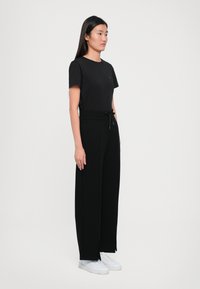 Zwarte t-shirt met korte mouwen, gecombineerd met hoge zwarte wijde broek met een trekkoord in de taille, gedragen met witte sneakers.