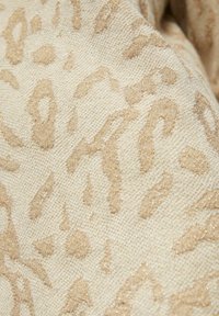 Béžová látka s jemným leopardím vzorem v lesklém zlatém provedení, která má texturovanou vazbu, jež dodává hloubku a rozměr.
