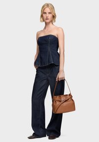 Granatowy, bezramiączkowy top peplum z denimu w połączeniu z szerokimi dżinsami. Modelka trzyma brązową skórzaną torbę z ozdobną klamrą.