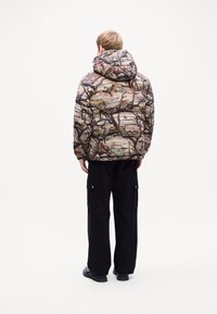 Polstret jakke med camouflageprint i jordfarver. Har hætte og lange ærmer, parret med sorte cargo-bukser.