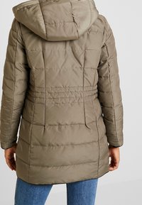 Olijfgroene, gewatteerde pufferjack met een capuchon, voorzien van een verstelbare taille en ribbeltextuur. Het heeft lange mouwen en een afgeronde zoom.