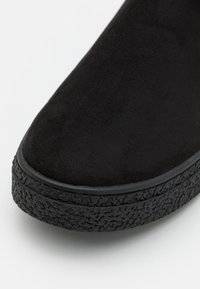 Black suede ankle boot with a thick textured outsole, rounded toe, and smooth upper surface, featuring a seamless design.