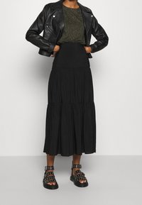 Černá kožená motorkářská bunda přes top s leopardím potiskem, doplněná černou maxi sukní s volány a černými sandály s cvočky.