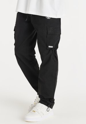 Schwarze Cargo-Hose mit elastischem Bund und verstellbaren Bündchen, ausgestattet mit mehreren Taschen und einem Stoff-Logoschild am Oberschenkel.