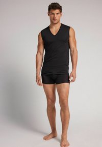 Czarny bezrękawnik z dekoltem w kształcie litery V, w połączeniu z dopasowanymi czarnymi szortami. Gładki materiał, minimalne detale i lekka konstrukcja.