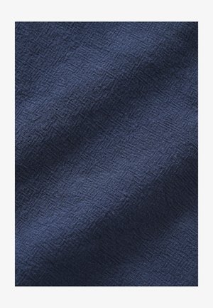 Donkerblauwe stof met subtiele diamantweefstructuur, met zachte plooien en lichte schaduwen over het oppervlak.