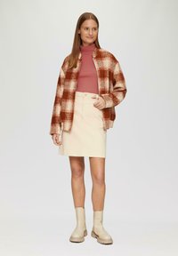 Wollen mengsel, rood en crèmekleurig geblokt jasje, gecombineerd met een roze coltrui en een crèmekleurige denim rok. Beige enkelboots maken de outfit compleet.