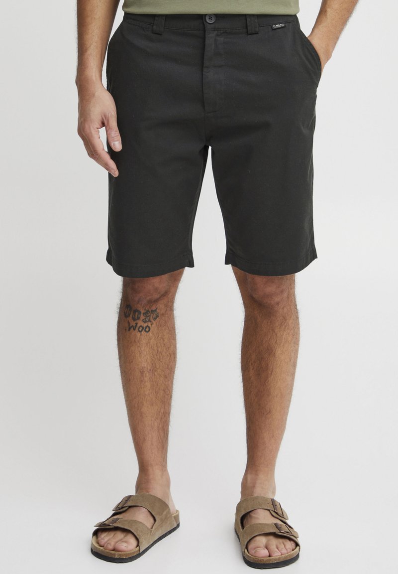 Crne pamučne kratke hlače sa zatvaranjem na dugme i petljama za remen, sa slim fit krojem, bočnim džepovima i okrenutim rubom. Na nogama su smeđi sandali.