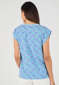 Top a maniche corte con un motivo floreale blu, verde e bianco, dal taglio morbido, collo rotondo e orlo leggermente curvato.