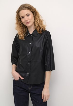 Black faux leather shirt with a button-up front, short sleeves, and stud accents on the collar. Smooth texture and tailored design.