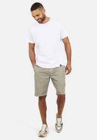 T-shirt bianco in cotone, pantaloni corti khaki e sneaker grigie. La T-shirt ha un coltondo; i pantaloni corti sono alla lunghezza del ginocchio con tasche laterali.