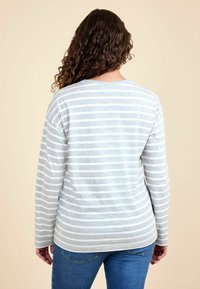 Hosszú ujjú, szürke csíkos póló puha anyagból, laza szabással és kerek nyakkivágással, kék farmernadrággal párosítva.