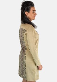 Vestido de manga larga beige que presenta un panel de piel de serpiente texturizado y con un patrón en la parte posterior. Tela suave con detalles visuales contrastantes.