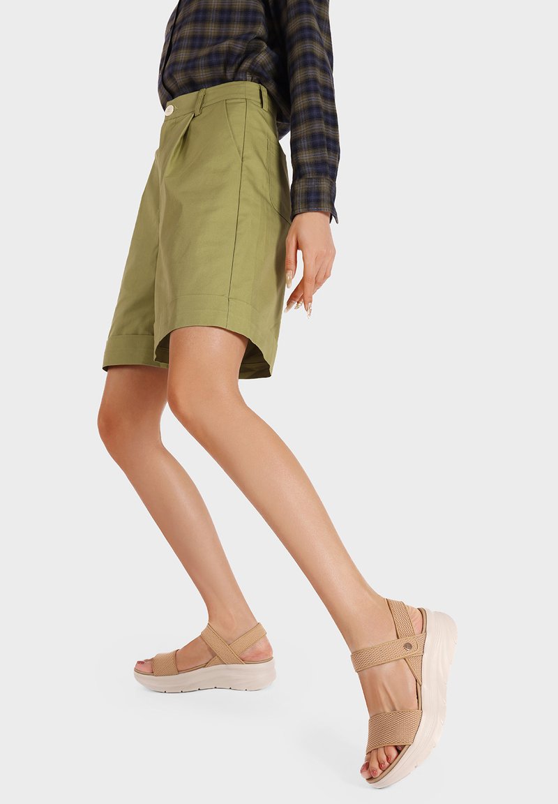 Pantaloni corti verde chiaro con tasche laterali e orlo piegato, abbinati a sandali beige con una fascia testurizzata e una suola spessa.