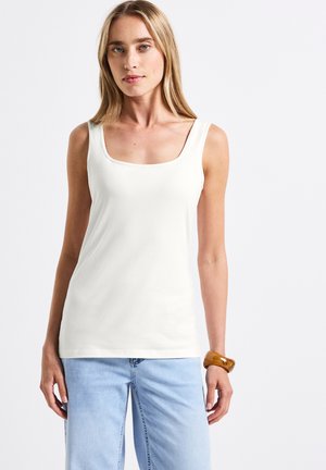 Witte aansluitende tanktop met een vierkante halslijn en brede bandjes, gecombineerd met lichtblauwe wijde jeans. De stof lijkt glad en rekbaar.