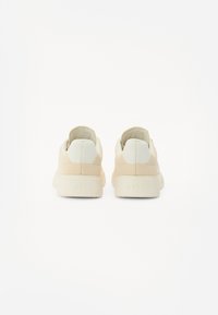 Sneaker beige con una toma in rete testurizzata e suola in gomma, caratterizzati da un sottile design bicolore e branding embossato sul tallone.