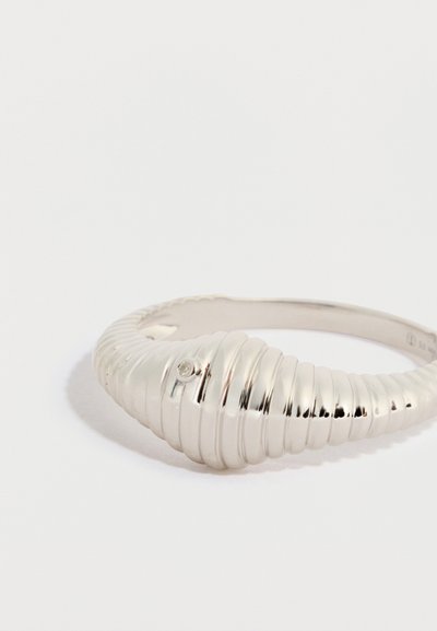 Anello d'argento con un design rigato, caratterizzato da una forma liscia e curva e da un piccolo dettaglio con pietra preziosa, che mette in risalto una texture metallica lucida.