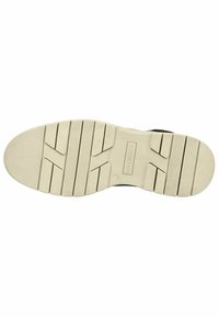 Suela de un zapato negro con una base de goma blanca texturizada, con ranuras horizontales y verticales para tracción y áreas reforzadas.