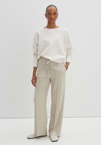 Maglione color avorio, vestibilità rilassata con scollatura ampia. Pantaloni beige su misura con vita regolabile. Stivali color crema con suole nere.