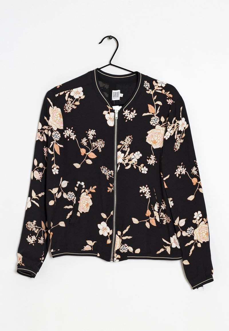 Czarna kurtka na zamek z jasnoróżowymi i beżowymi kwiatowymi wzorami, wisząca na czarnym wieszaku na białym tle.