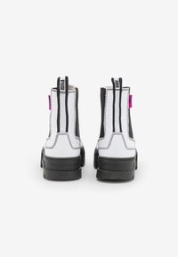 Černobílé kotníkové boty s elastickými bočními panely, koženkovým materiálem, silnou podrážkou a růžovým poutkem na patě.