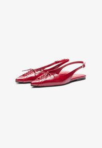 Punat punotettu punainen nahkainen slingback-tasapohjapohja, jossa on terävät varpaat, nauhoitusyksityiskohta edessä ja matala, tasapohjainen kantapää. Sujuva pintakuvio ja tyylikäs muotoilu.