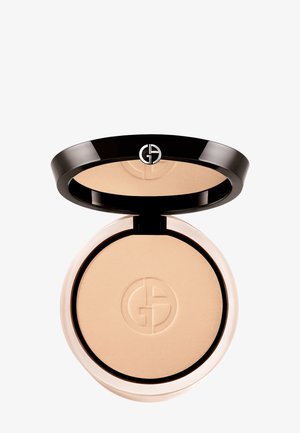 Trykt pudder kompakt med et svart, skinnende lokk, med en sølvfarget logo. Kremet beige puder inne med en jevn tekstur.
