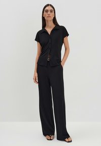 Zwarte korte mouwen overhemd met knopen, gecombineerd met losse zwarte broeken, met een gladde textuur en een minimaal ontwerp.