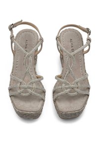 Beige platform sandalen met kruisriemen, versierd met zilveren accenten. Zacht suède textuur met een geweven espadrillezool. Verstelbare enkelriem.
