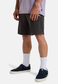 Donkergrijze shorts met een losse pasvorm, gecombineerd met marineblauwe sneakers en witte enkelkousen. De shorts hebben zijzakken en een merkdetail.