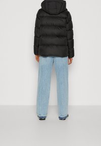 Veste matelassée noire avec motif matelassé horizontal, capuche ajustable et poignets élastiques. Associée à un jean large bleu clair et des chaussures noires.