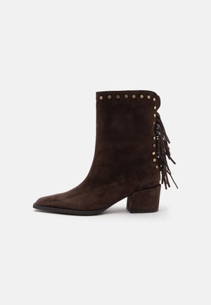 Dunkelbraune Wildleder-Stiefelette mit niedrigem Blockabsatz, Metallnieten am oberen Rand und Fransen am hinteren Teil.