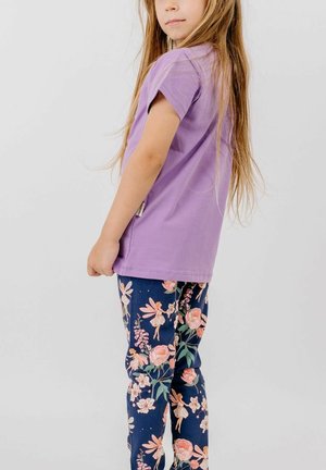 Child with long hair wearing a purple shirt and navy leggings with a floral and fairy pattern, standing sideways against a plain background.