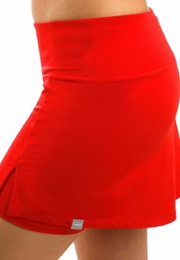 Falda atlética roja con cintura ajustada, hecha de una tela elástica. Presenta una abertura lateral para mayor libertad de movimiento y una pequeña etiqueta de la marca en el dobladillo.