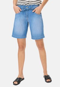 Shorts en denim bleu clair avec un design classique à cinq poches, fermeture à bouton sur le devant et ourlet retroussé. Portés avec des sandales à glissière noires.